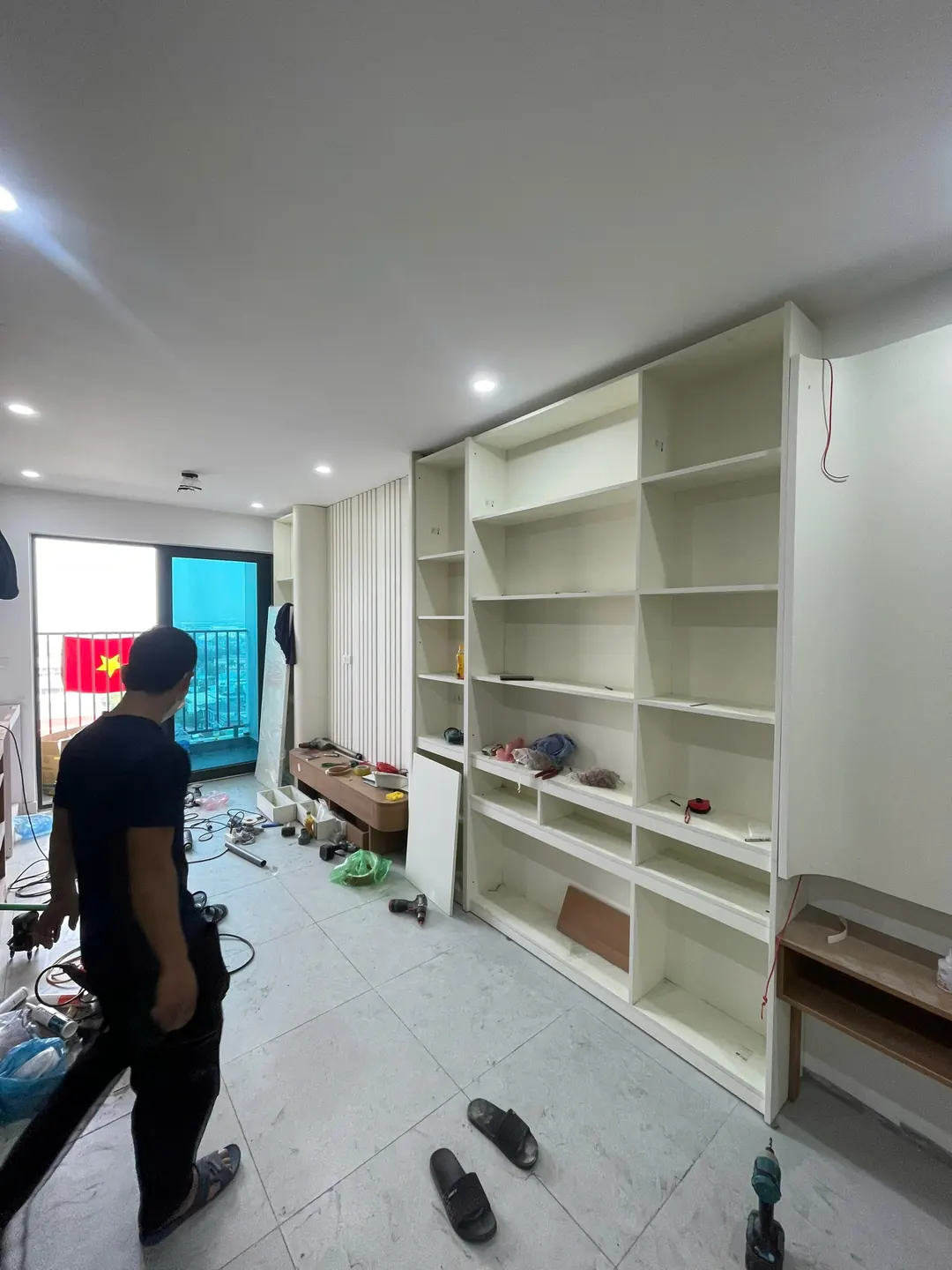 Tủ sách trắng kịch trần nhiều ô trong phòng khách căn hộ, thợ đang lắp