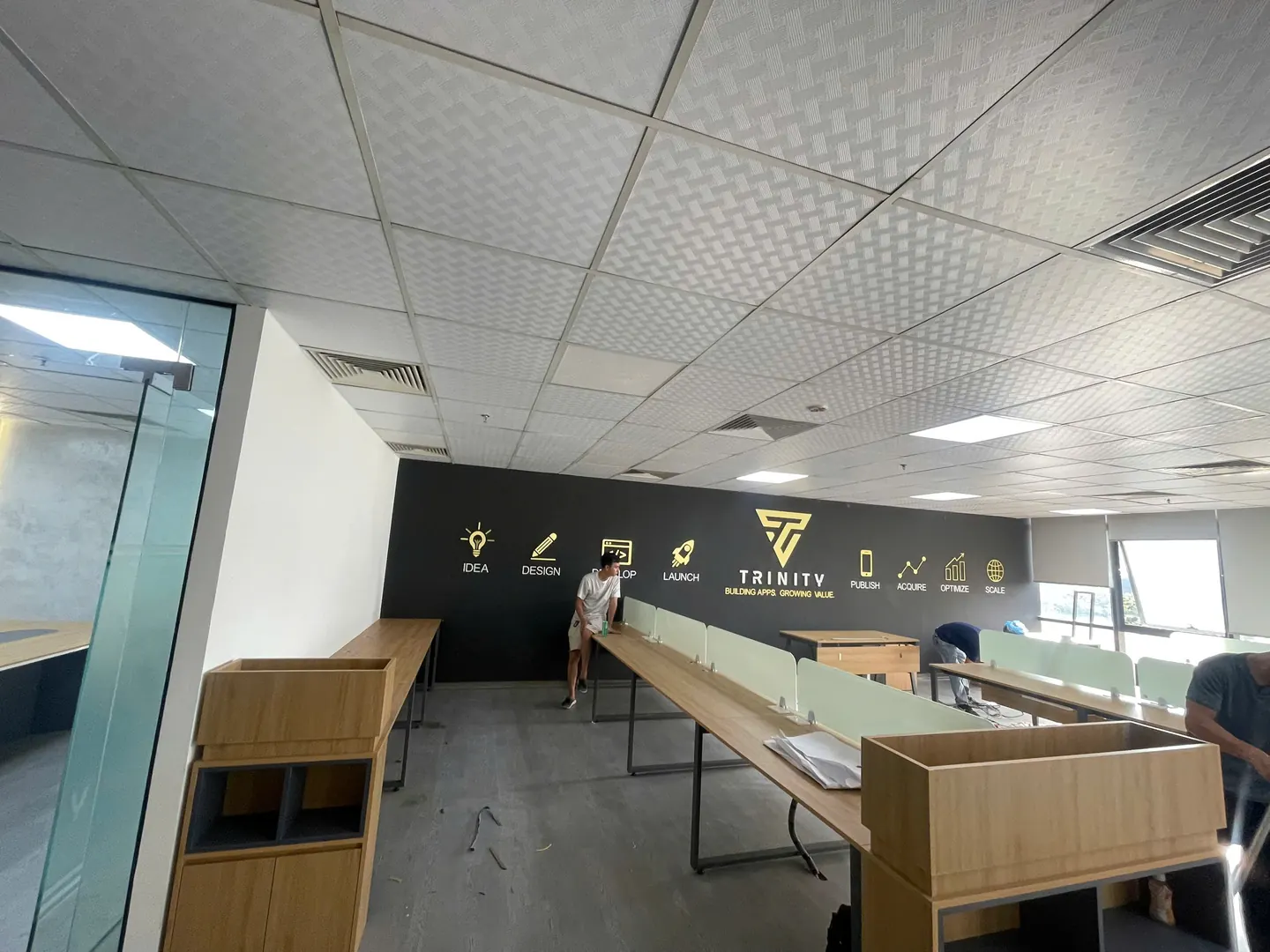 Thợ lắp cụm bàn làm việc dài có vách ngăn trong văn phòng, tường logo ở cuối phòng