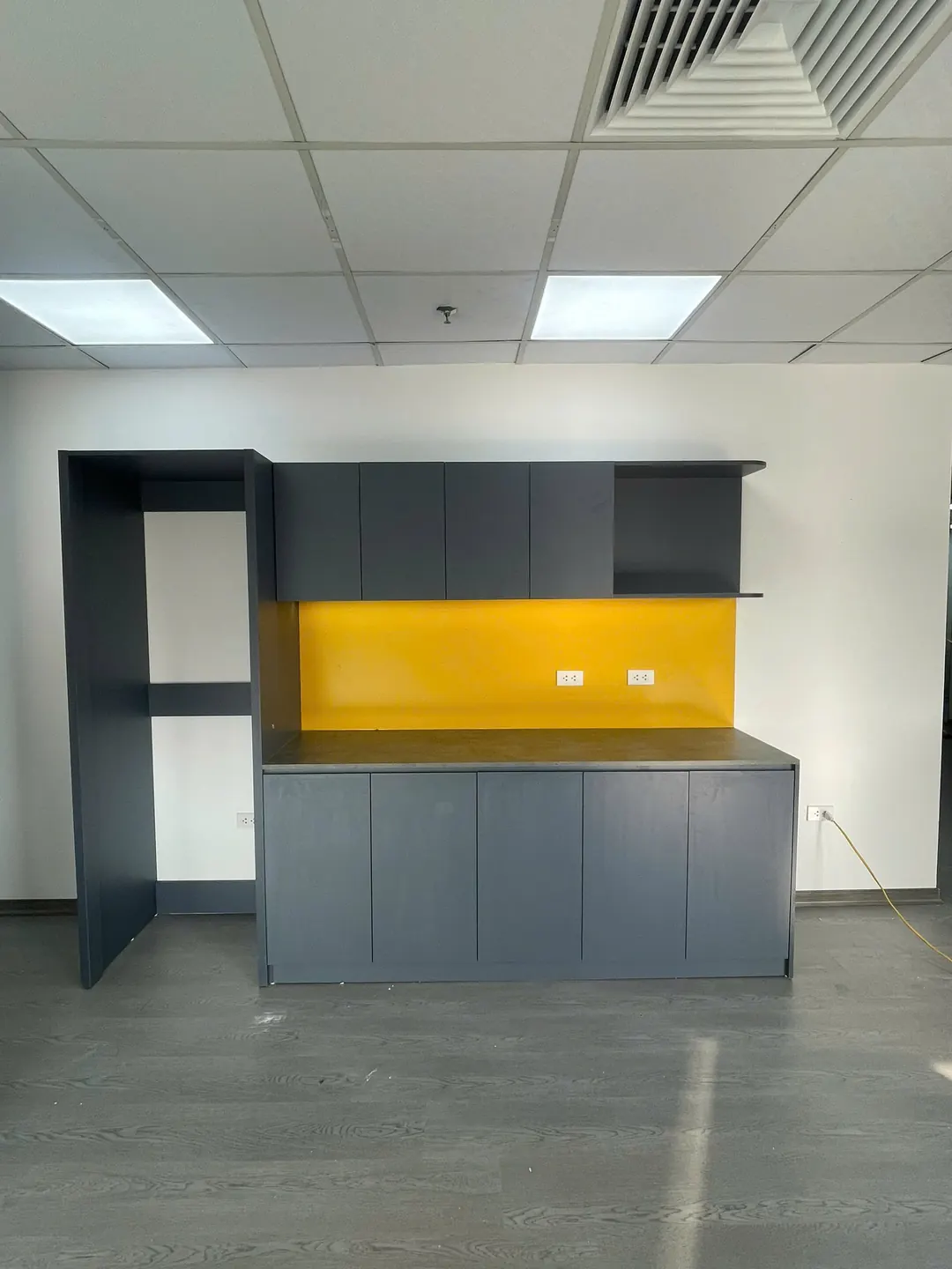 Tủ pantry văn phòng cánh xám đậm, tấm ốp tường màu vàng, tủ cao bên cạnh
